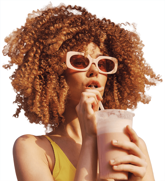 Woman with curly hair and sunglasses sipping a drink